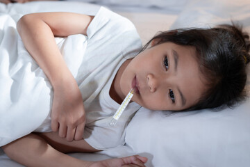 Obraz na płótnie Canvas Sick asian child girl is sleeping on bed and measuring her body temperature with thermometer in the bedroom at home.