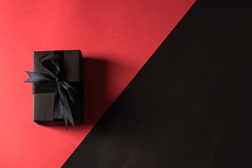 Black Friday sale shopping concept, Top view of gift box wrapped in black paper and black bow ribbon, studio shot isolated on red and dark background