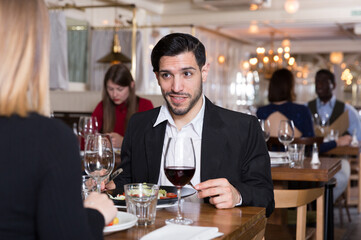 Happy handsome man with girlfriend enjoying evening meal in cozy restaurant