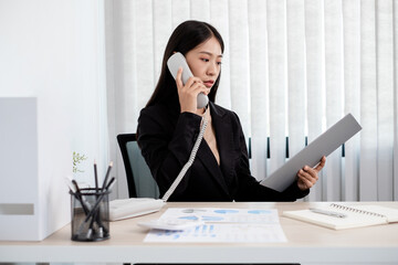 Asian businesswoman talking on the phone and working with a cheerful and happy smile while working at the office