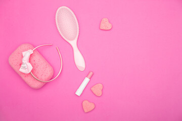 Obraz na płótnie Canvas Flat lay of pink female bathroom accessories lying on a pink field. Accessories of every woman including lipstick, hairbrush, sponge, soap, and headband