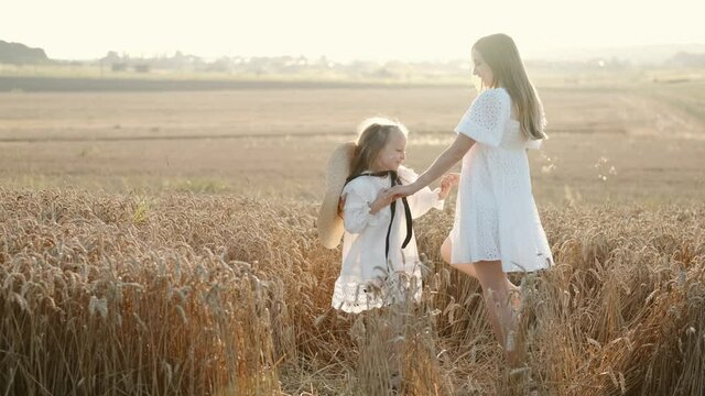 Mother and daughter in a white dress whirl in a mown field