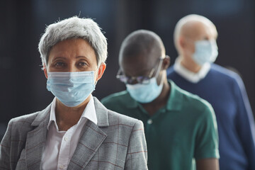 Portrait of mature woman in protective mask looking at camera while standing in a queue