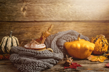 Autumn concept, still life of pumpkin spice latte with whipped milk cream and cinamon. Colorful pumpkins and dry leaves. Old natural wood backround