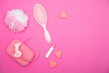 Flat lay of pink female bathroom accessories lying on a pink field. Accessories of every woman including lipstick, hairbrush, sponge, soap, and headband