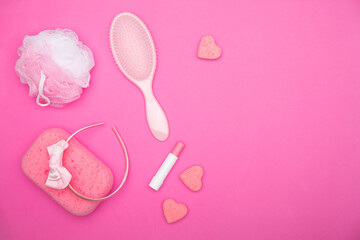 Flat lay of pink female bathroom accessories lying on a pink field. Accessories of every woman including lipstick, hairbrush, sponge, soap, and headband