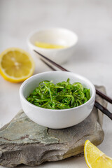 Croped photo of green wakame seaweed salad with chopstick and lemon at the restaurant