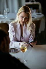 Beautiful businesswoman dressed in the suit drinking wine. Businesswoman using the phone in the restaurant..
