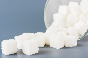White sugar cube sweet food ingredient spilled out of the glass, studio shot isolated on a gray background, Minimal health high blood risk of diabetes and calorie intake concept