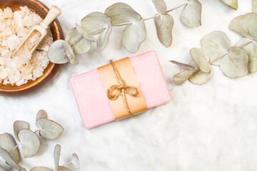 Jabón rosa junto a hojas de eucalipto y sales minerales sobre un fondo de mármol liso. Vista...