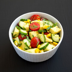 Fresh Avocado Tomato Salad in a bowl on a black surface, side view. Close-up.