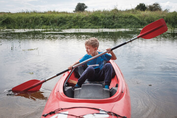Young boy with the oar in a kayak on a small river.