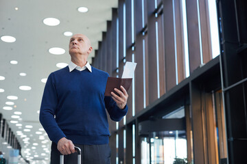 Fototapeta premium Mature man holding tickets while going along the airport and looking for the departure gate