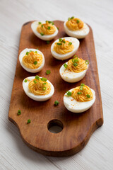 Homemade Deviled Eggs with Chives on a rustic wooden board on a white wooden table, side view.