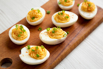 Homemade Deviled Eggs with Chives on a rustic wooden board on a white wooden background, low angle view. Close-up.