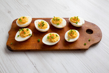 Homemade Deviled Eggs with Chives on a rustic wooden board on a white wooden table, low angle view.