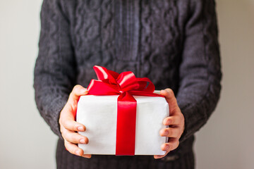 A man in a dark gray sweater is holding a gift box with a red ribbon