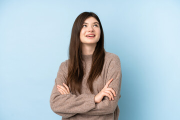 Young Ukrainian teenager girl wearing a sweater over isolated blue background looking up while smiling