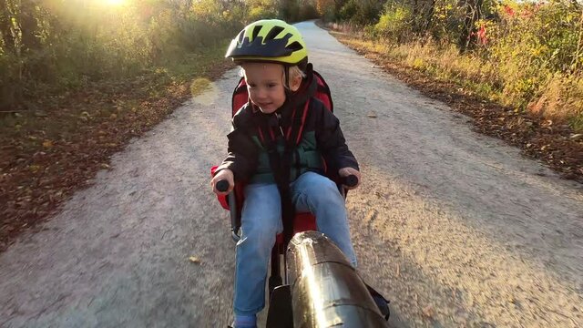 Family having fun outdoors, riding a trail in autumn fall season. Child is pedaling, close up, POV. Parents riding a bicycle and towing a bike trailer with her child. Active lifestyle, adventure 