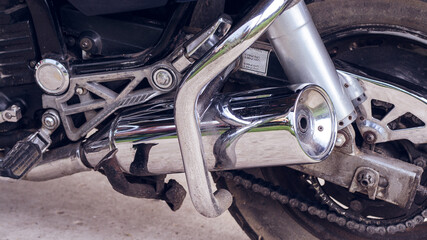 The back of a sports motorcycle, bottom side view, close-up. Exhaust pipe, shock absorber, engine, rear wheel, chain, motorcycle crash bars. Road fast motorcycle in the garage for repair, maintenance