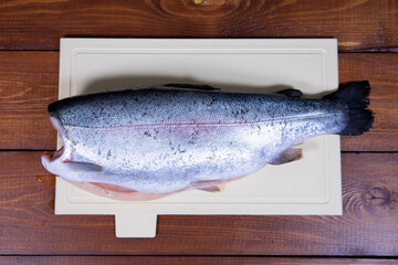 A headless peeled trout lies on a chopping Board against a dark wooden background
