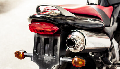Chrome exhaust pipe and brake light of motorcycle with red seat and turn signals close-up. Place under license plate of sports bike in garage. Rear view, wheel of classic road bike. Back view side