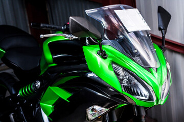 Front end of beautiful green sport bike with price tag in showroom in store. Photo of bright fast bike with windshield in front. Road bike in garage after repair. Dual headlights mirrors, front wheel