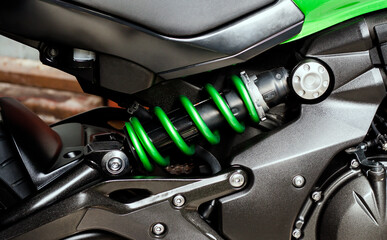 Green shock absorber with spring and black cylinder of engine of motorcycle closeup. Part sport bike, side view. Motorcycle chassis, internal combustion engine and frame bike.