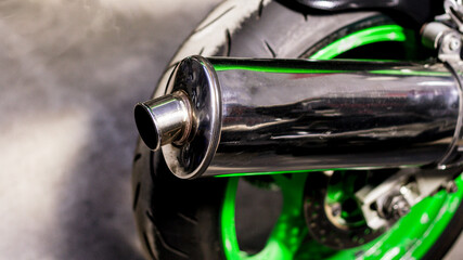 Chrome exhaust pipe, brake disc, green alloy wheel, rear wheel motorcycle. Back of modern sports bike, bottom side view, close-up.  Road fast motorcycle in garage for repair, maintenance. Moto tire