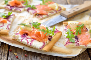 Elsässer Flammkuchen-Schnitten mit Räucherlachs und Rucola rustikal serviert - Tarte Flambée from Alsace with smoked salmon and rocket leaves 