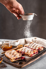 Chef sprinkles icing sugar on a sweet pie with berries, vertical photo