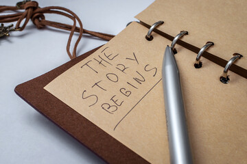 Blank notebook in a leather case, on the page with a pen it is written: The story begins. The...