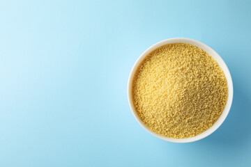 Bowl with raw couscous on blue background