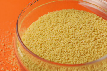 Glass jar with couscous on orange background