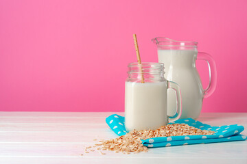 Oat milk in glassware and dry oat flakes on pink background