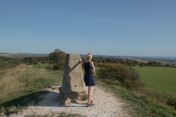 Adult Caucasian Female Leaning Against the Trig Point on the Top of Devil's Dyke Hill with the City of Brighton in the Distance on the South Downs in Rural West Sussex, England, UK