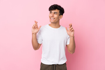 Young Argentinian man over isolated pink background with fingers crossing