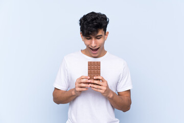 Young Argentinian man over isolated blue background eating a chocolate tablet
