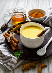 Yellow turmeric latte drink. Golden milk with cinnamon, turmeric, ginger  and honey over white wooden background.