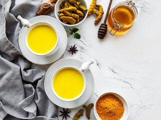 Yellow turmeric latte drink. Golden milk with cinnamon, turmeric, ginger  and honey over white marble background.