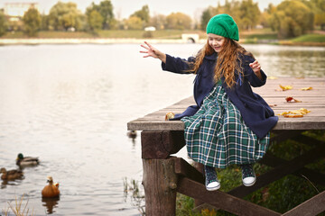 Naklejka premium Irish little red haired girl outdoor photo on fall lake landscape background feeding ducks