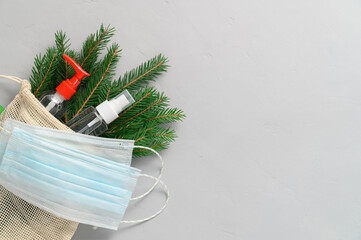New normal christmas concept. Eco bag with fir branches, medical masks, sanitizer bottles on a gray...