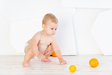 a small child a boy six months old plays on the floor in a bright white room in diapers with lemons and oranges