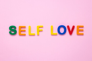Self love text on pink paper background made from colorful plastic letters. Multicolored inscription on the banner. Title, headline. The psychology concept. The message on the poster, the words.