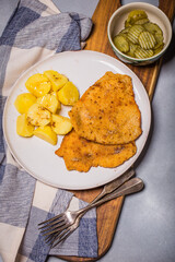 Chop pork cutlets , served with boiled potatoes and salad of pickled cucumbers on wooden board. A typical Polish dinner (kotlet schabowy).
 - obrazy, fototapety, plakaty