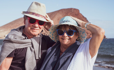 A smiling senior couple with hats enjoying the winter sea on a windy day. Active elderly pensioner people