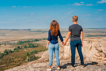 Rear view of a romantic couple a man and a woman standing on the edge of a cliff on a White rock in Crimea with a view of the rural landscape