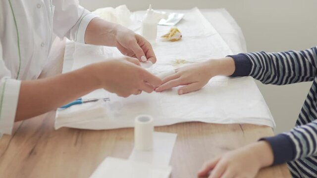 A female doctor makes a finger bandage to a teenage boy.
