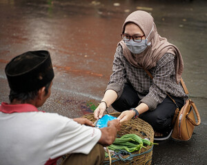 Muslim women donating masks to vegetable traders who do not wear them while giving an example to always wear a health cloth mask when in traditional markets.