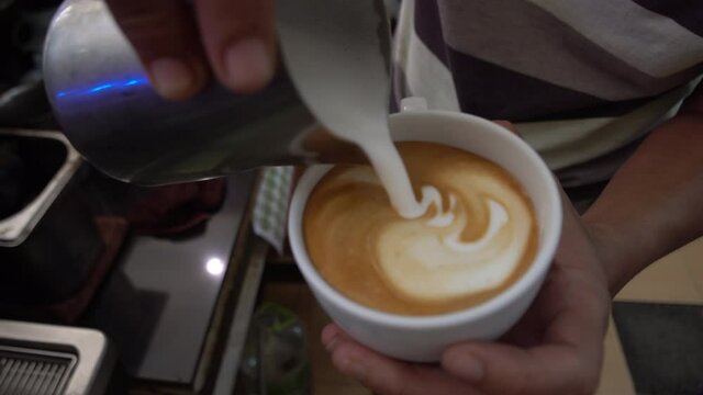 Close up barista hand making coffee art in bar. How to making coffee art with hot milk, Steamed milk pouring to coffee for coffee art. Industrial food and drink concept.